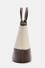 Bolso tipo bucket de diseño estructurado, confeccionado en combinación de canvas color crudo y cuero sintético marrón. Presenta doble asa de mano, pespuntes a contraste y base reforzada.