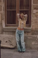 Top de encaje color crudo, con cuello subido, mangas largas abullonadas, costuras marcadas estilo corsetero y cierre frontal con ganchos metálicos.