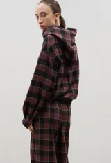 Camisa de manga larga con capucha, confeccionada en tejido liviano con estampado a cuadros. Presenta cierre frontal con botones y lazo regulable en la cintura.