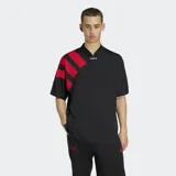 Remera Adidas de estilo futbolístico inspirada en los años 90, color negro con cuello en pico y tres bandas diagonales rojas sobre el hombro derecho. Presenta un corte holgado y logo de la marca en el centro del cuello.
