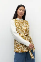 Chaleco capitoneado color crema con estampado floral en tonos marrones. Cuenta con cuello mao, cierre frontal con botones grandes y lazo en la misma tela para acentuar la cintura.