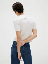 Top corto de punto acanalado color blanco, con cuello tipo chomba y cierre frontal abotonado.