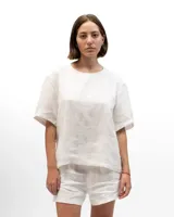 Remera de lino con corte holgado, cuello redondo y mangas cortas. Presenta un diseño minimalista con detalle de botones en la espalda.