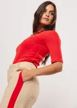 Pantalón beige de tiro alto con bolsillos delanteros y traseros, cierre frontal con cremallera y botón, y detalle de pespuntes rojos en los laterales.