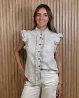 Musculosa de lino color beige, sin mangas, con cuello alto, cierre frontal de botones y detalles de volados en la botonera y sisas.