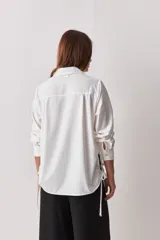 Camisa celeste de calce relajado, con cuello camisero, bolsillo aplicado en el pecho y mangas largas con puños abotonados. Cuenta con lazos ajustables en los laterales para fruncir y regular la silueta.
