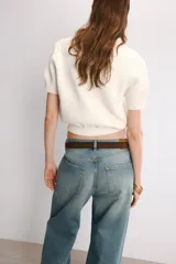 Chaqueta corta de punto texturizado color blanco roto, con escote en V, manga corta y cierre frontal con tres botones metálicos dorados en forma de estrella de mar.