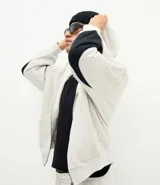 Buzo con capucha y cierre frontal, confeccionado en tejido fleece de algodón y poliéster. Presenta un diseño bicolor con cuerpo en gris melange y paneles laterales en las mangas de color negro, bolsillos frontales, y puños y ruedo en rib.