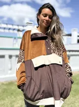 Buzo de estilo canguro con diseño patchwork que combina paneles de terciopelo color caramelo, gamuza marrón chocolate y estampado animal print de leopardo. Presenta cuello alto con cierre de botones a presión, un bolsillo frontal tipo sobre con solapa y puños elásticos.
