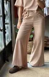 Pantalón de corte palazzo en color beige, confeccionado en tela elastizada, con tiro alto y diseño amplio en las piernas.