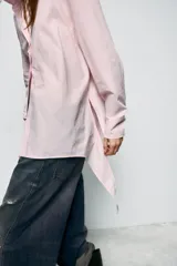 Camisa de corte oversize con cuello solapa y escote en pico. Presenta manga larga con puños abotonados, cierre frontal con botones y detalle de lazada ajustable en la espalda.