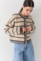 Cardigan rojo de punto amplio con rayas horizontales azul marino, mangas largas abuchonadas y cuello redondo. Cuenta con cierre frontal de botones, detalles en los bordes y un pequeño bordado de raqueta de tenis en el pecho.