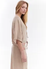 Blusa de lino italiano color beige, de manga corta, con escote en V y cierre frontal mediante lazos o moños.