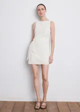 Vestido corto blanco sin mangas, con cuello redondo y detalle de lazo lateral en la cintura.