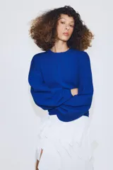 Jersey de punto color azul, con cuello redondo, mangas largas amplias y costuras marcadas en el frente.