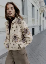 Campera puffer color beige con estampado floral y de logotipos en tonos marrones y grises, cuello alto y cierre frontal con cremallera.