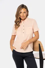 Camisa de lino y algodón de manga corta en color salmón, con cuello camisero, cierre frontal de medio botón con botones metálicos personalizados, dos bolsillos con solapa en el pecho y dobladillo en las mangas.