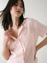 Camisa de manga corta para dormir confeccionada en broderie de algodón, con cuello solapa y cierre frontal con botones. Presenta un bolsillo aplicado en el pecho.