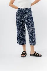 Pantalón de corte culotte y tiro medio, confeccionado en viscosa con estampado de hojas blancas sobre fondo color miel. Presenta una silueta amplia y fluida, con cintura elástica en la parte posterior y bolsillos laterales.