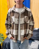 Sobrecamisa de paño con diseño de cuadros grandes en tonos marrón y beige. Presenta cuello clásico, cierre frontal con botones, mangas largas con puños abotonados y dos bolsillos frontales con solapa.