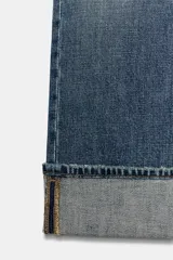 Jeans de mezclilla de tiro bajo y corte recto, con diseño de cinco bolsillos, trabillas para cinturón y dobladillo con vuelta ancha. Presenta un lavado azul medio con efecto desgastado.