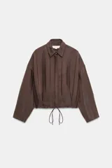 Chaqueta de cuello solapa y manga larga, confeccionada en tejido jacquard con diseño de rayas verticales. Presenta cierre frontal con botones y bajo ajustable mediante cordones.