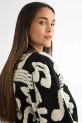 Saco tipo cardigan de punto, color negro con diseño de notas musicales y compases en color crema. Presenta cierre frontal con botones, cuello en V y puños acanalados.