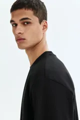 Remera negra de punto de algodón de peso medio, cuello redondo ribeteado y hombros caídos con corte relajado.