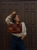 Cartera de hombro confeccionada en cuero y gamuza con diseño de damero, combinando paneles de texturas lisas y aterciopeladas. Presenta una manija trenzada y detalles de costuras artesanales en los laterales.