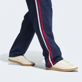 Pantalón deportivo Adidas Firebird azul marino con rayas rojas y blancas en los laterales y logo dorado bordado. Confeccionado en tejido de tricot de poliéster reciclado, con corte clásico y cintura elástica ajustable con cordón.