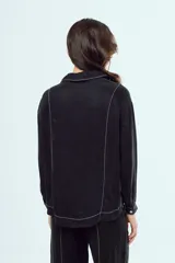 Camisa negra de manga larga con cuello en V, cierre frontal de botones y costuras decorativas en contraste de color blanco.