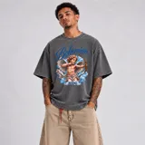 Remera de algodón de corte oversize, con efecto de lavado ácido (acid wash) en color gris oscuro. Presenta un gran estampado frontal que muestra un querubín con un arco y flecha sobre un fondo de nubes celestes, acompañado por el texto "Bohemian" y "BHDG" en tonos azules.