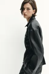 Chaqueta de efecto piel con cuello solapa, manga larga y cierre frontal con cremallera. Presenta cintura elástica que entalla la silueta y bolsillos decorativos en el frente.