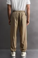 Pantalón jogger de corte regular confeccionado en tejido técnico ligero, con cintura elástica, bolsillos laterales con cierre y puños elásticos en los tobillos.