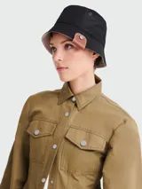 Sombrero tipo bucket reversible, negro de un lado y beige del otro, con detalle de cuero marrón con botón metálico en el lateral.