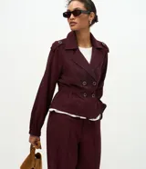 Campera de estilo trench corto en color bordó, con cuello solapa, cierre cruzado con botones, detalle de charreteras en los hombros, cintura elástica marcada y mangas largas con puños ajustados.