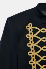 Blazer crop color negro, con cuello subido, manga larga y cierre frontal con botones ocultos. Presenta detalles de alamares bordados a contraste en color dorado en el frente y en los puños.