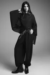 Capa negra de cuello redondo con detalle de tachas plateadas en el ruedo y pañuelo tipo bufanda integrado en el mismo tejido.