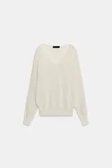 Jersey de punto de color blanco crudo, con escote en V y mangas largas con sisas amplias y puños elásticos acanalados.