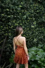 Vestido corto negro con estampado de plumas doradas, escote en V, breteles finos cruzados en la espalda, cut-outs laterales y volado en el ruedo.