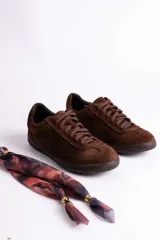 Zapatillas de gamuza color marrón con suela de goma color caramelo. Presentan cordones al tono y un detalle decorativo de pañuelo estampado atado en los laterales con esferas metálicas doradas.