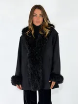 Chaqueta midi de color negro con solapas anchas y puños adornados con piel sintética de pelo largo. Presenta un diseño de corte recto y holgado.