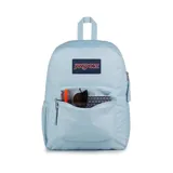 Mochila JanSport celeste con logo rectangular en azul marino y rojo. Tiene un compartimento principal grande, un bolsillo lateral para botella de agua, un bolsillo frontal con cremallera, tirantes acolchados y panel trasero acolchado.