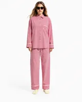 Pijama de dos piezas compuesto por una camisa de manga larga con botones y un bolsillo frontal, y un pantalón largo con elástico en la cintura. Ambas prendas presentan un diseño de rayas finas rojas y blancas con detalles de ribetes claros.