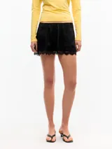 Minifalda de satén color negro, de tiro bajo y calce evasé, con cintura elastizada, cierre lateral invisible y detalle de encaje en el ruedo.