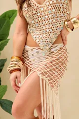 Top tipo halter de tejido crochet en color crudo, con escote en V y diseño triangular adornado con lentejuelas o apliques circulares iridiscentes.