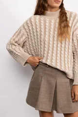 Sweater de punto con diseño de trenzas verticales, cuello alto y corte oversize. Presenta mangas largas con puños acanalados y una silueta relajada.
