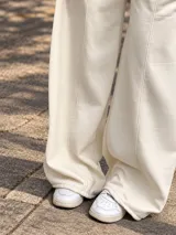 Pantalón jogger ancho color beige, con bolsillos laterales y pequeño bordado de un arco y flecha en la parte superior.