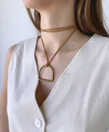 Colgante con cordón de cuero color camel y dije metálico dorado con forma de estribo.