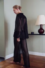 Blusa semitransparente negra de cuello solapa y manga larga, con cierre frontal de botones y detalles de bordados tonales en el ruedo y los puños.